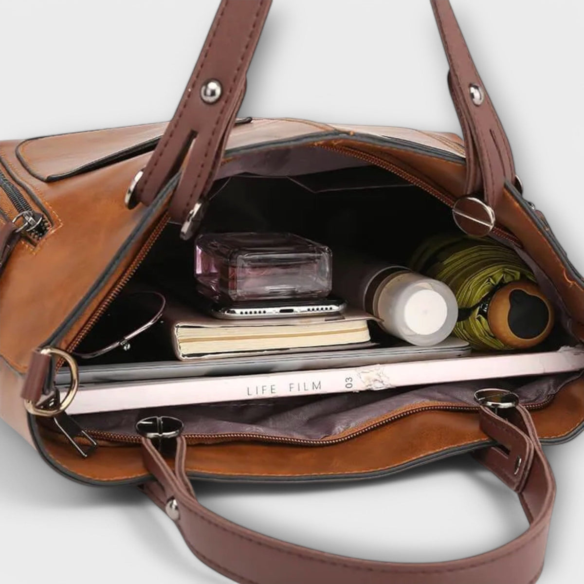 Open brown leather tote bag showing interior pockets and small items.