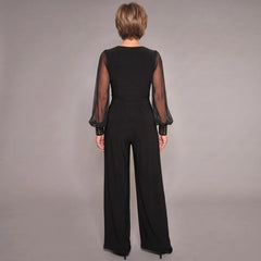 Black evening jumpsuit, back view: sheer sleeves, V-back, ruched waist, wide legs.