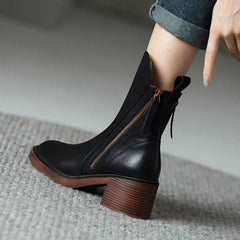 Black leather ankle boots with side zipper and tassel pull, block heel and brown sole edge.