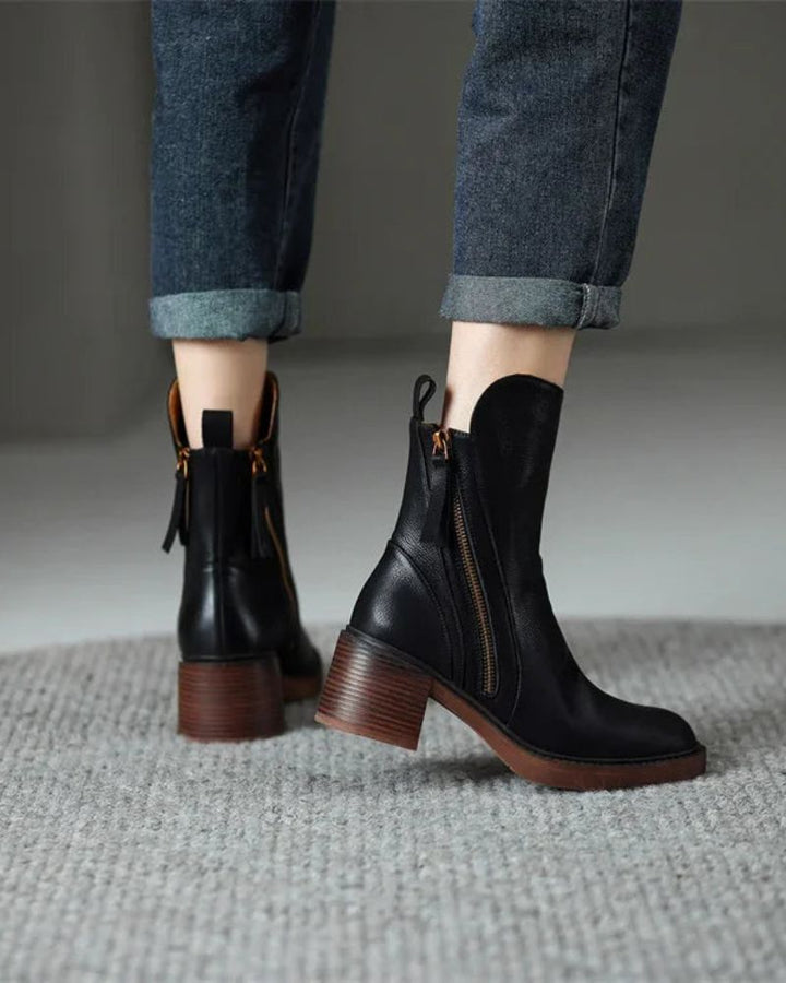 Black leather ankle boots with side zipper and tassel pull, block heel on textured rug.
