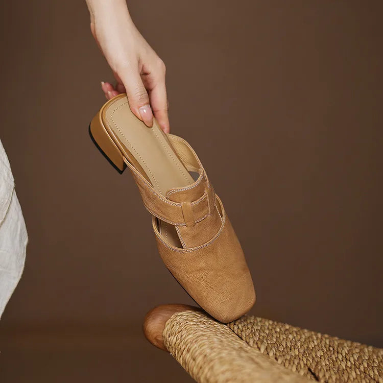Apricot leather mule held by hand; strap details and pointed toe visible