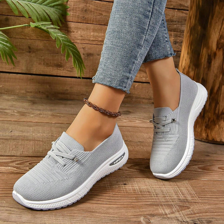 Gray lace-up sneakers with white soles, worn with denim cuffs