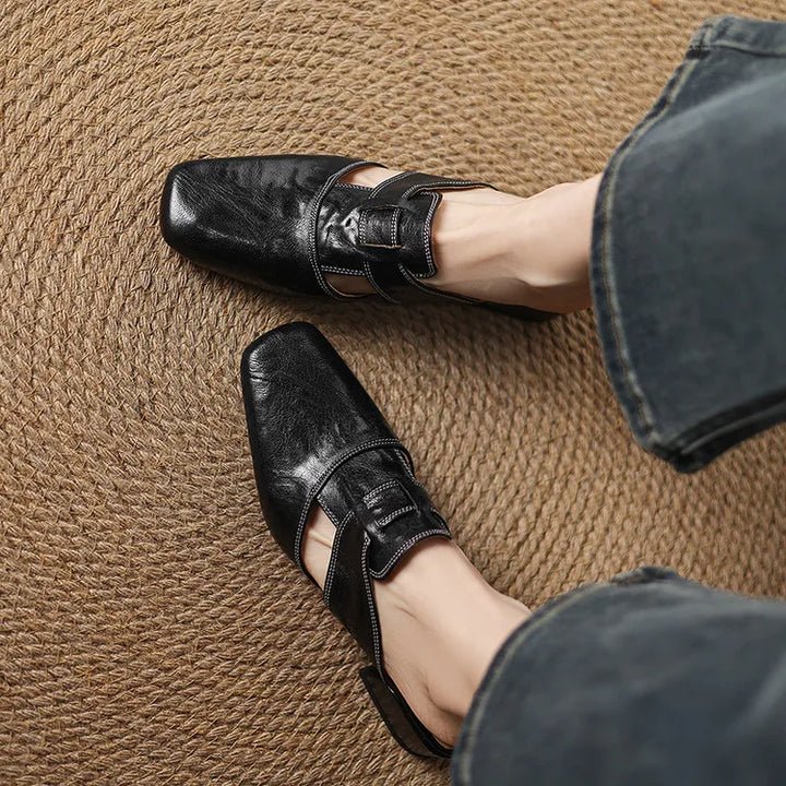 Black leather mules close-up with T-strap and buckle, low block heel