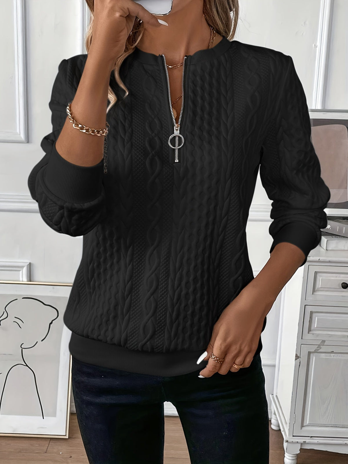 Black zip-up cable knit sweater with long sleeves and metal zipper pull at center front