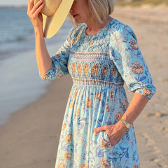 Sky blue floral midi dress with gathered waist and three-quarter sleeves; straw hat held up