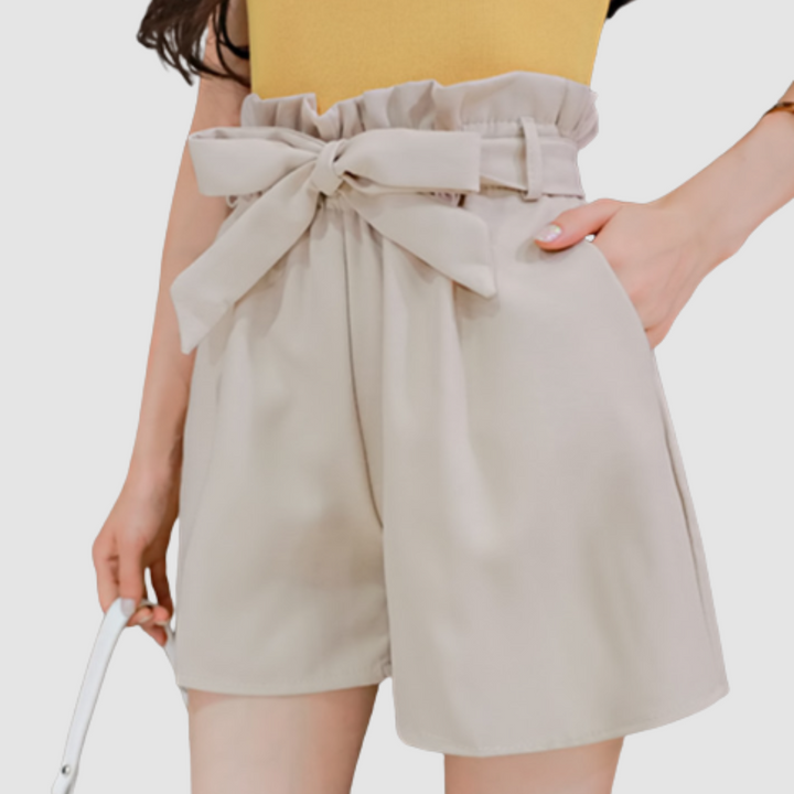 Beige paperbag waist shorts with tied bow and pleated elastic waistband.