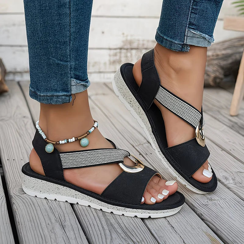 Black flat sandals with oval metal buckle, textured straps and beaded ankle band