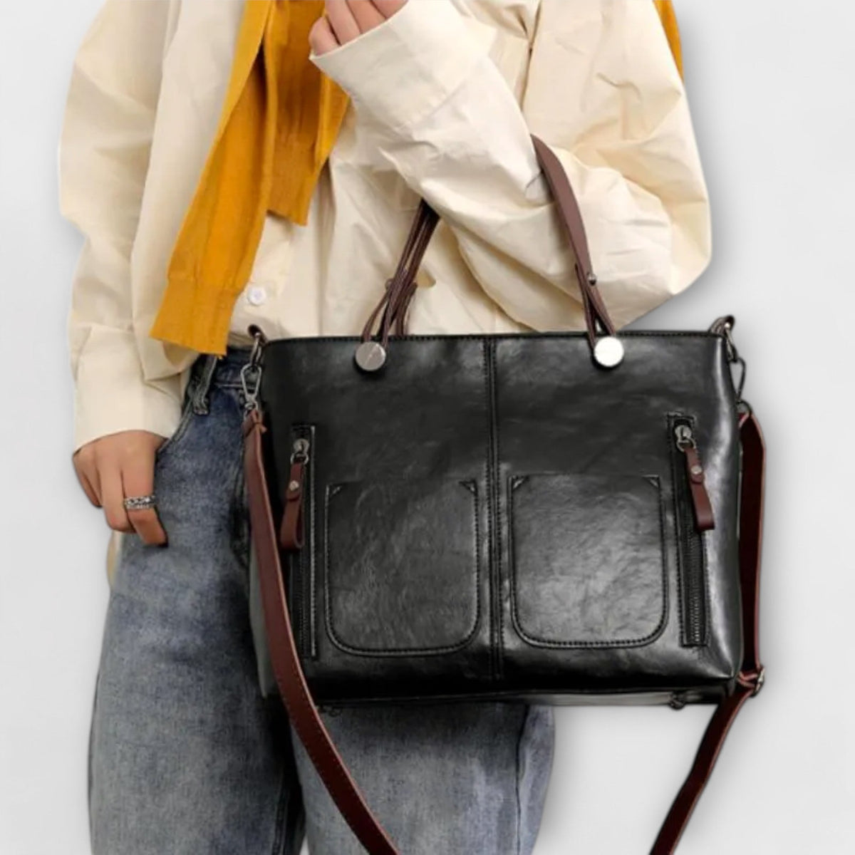 Black leather tote bag with top handles, front pockets, and crossbody strap.