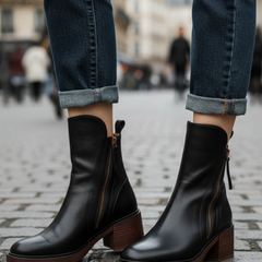 Black leather ankle boots with side zipper and tassel pull, block heel on city street.