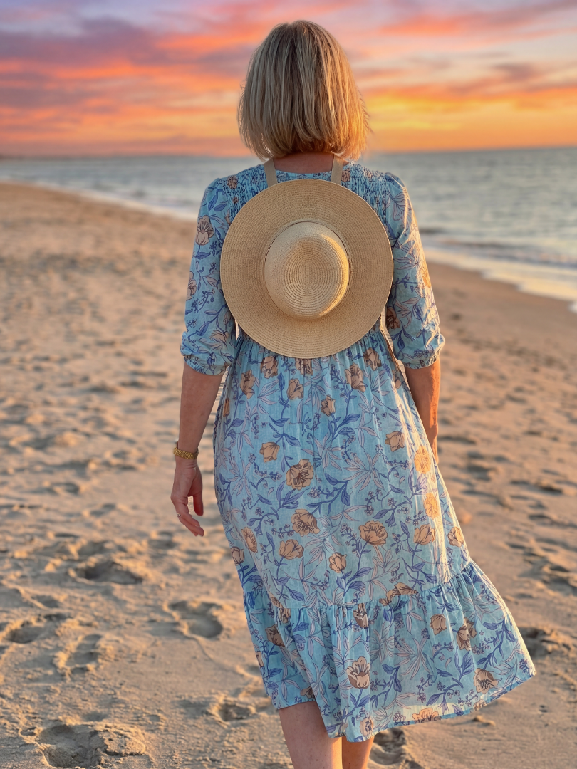 Sky blue floral midi dress back view with gathered waist and ruffled tiered skirt; straw hat