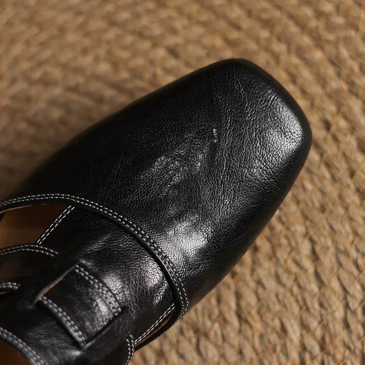 Black leather mule upper close-up with T-strap stitching and glossy finish