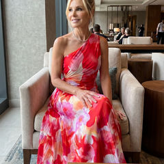 One-shoulder pleated midi dress with red, pink, and cream floral print, seated