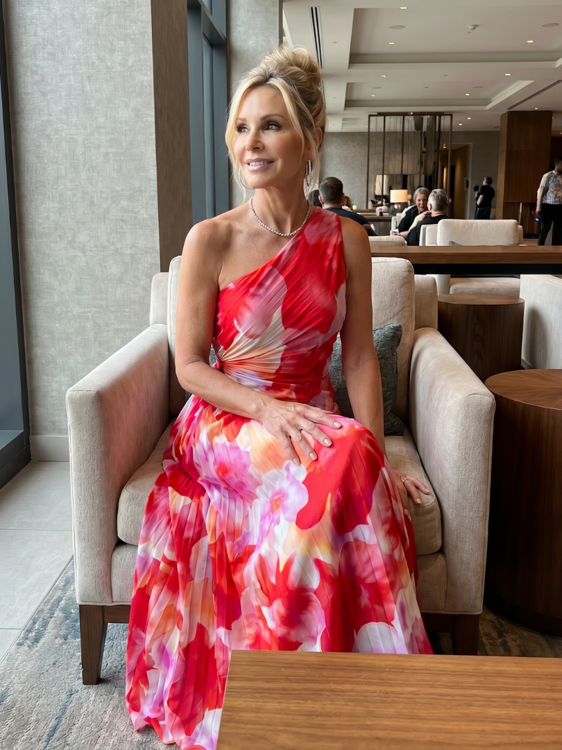 One-shoulder pleated midi dress with red, pink, and cream floral print, seated