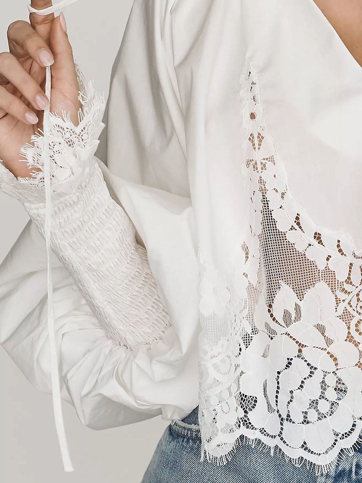 White lace blouse close-up with scalloped embroidery and drawstring ties at the hem