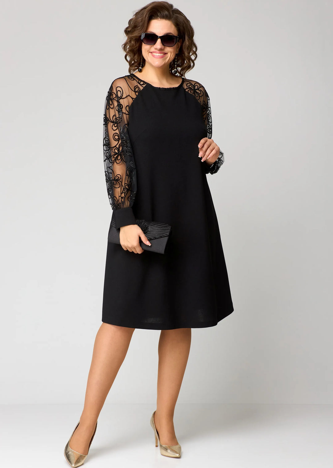 Black midi dress with sheer lace sleeves and long cuff detail; handheld clutch.