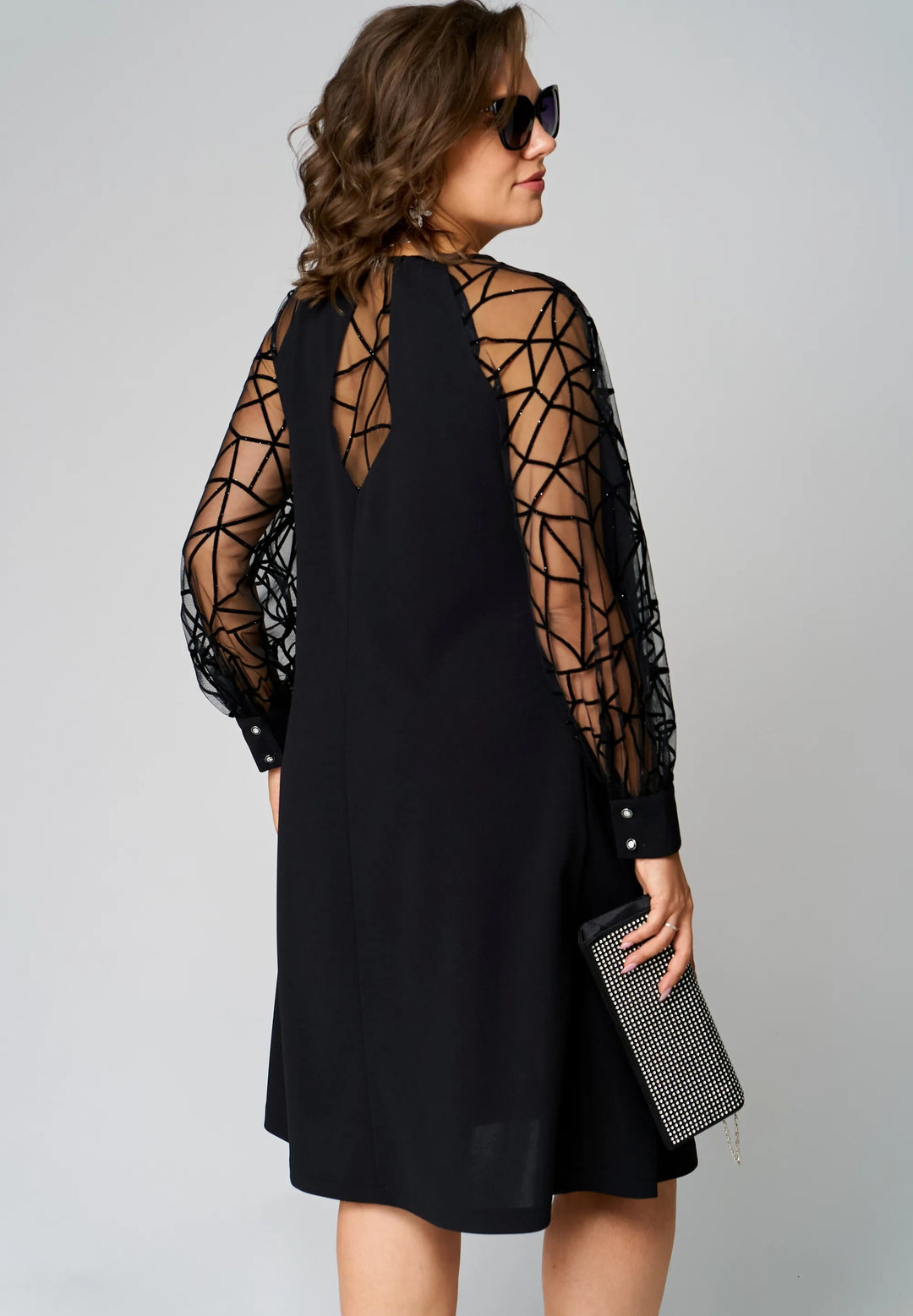Black tunic dress in back view with sheer lattice sleeves and knee-length hem