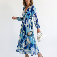 Althea long-sleeve graphic maxi dress with V-neck and gathered waist, blue tones; holding bag