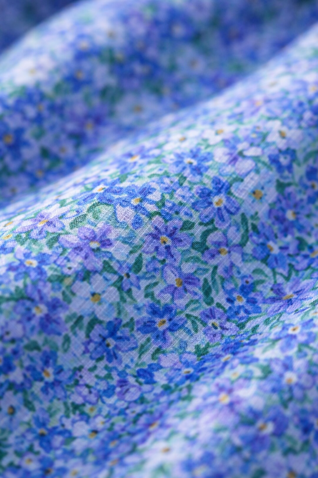 Blue floral fabric close-up with small blossoms and light green highlights