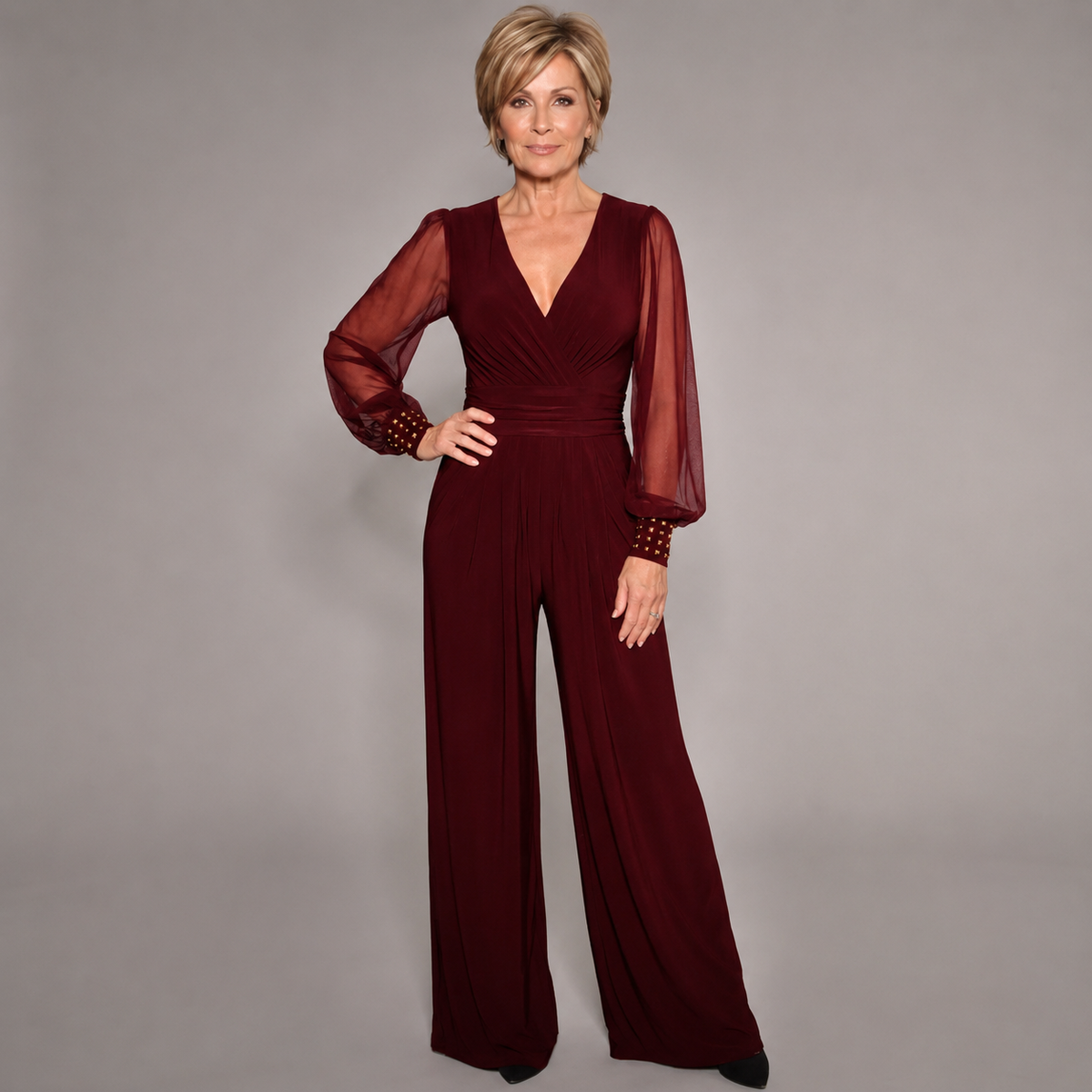 Burgundy evening jumpsuit with V-neck, ruched waist, sheer long sleeves, and wide legs.