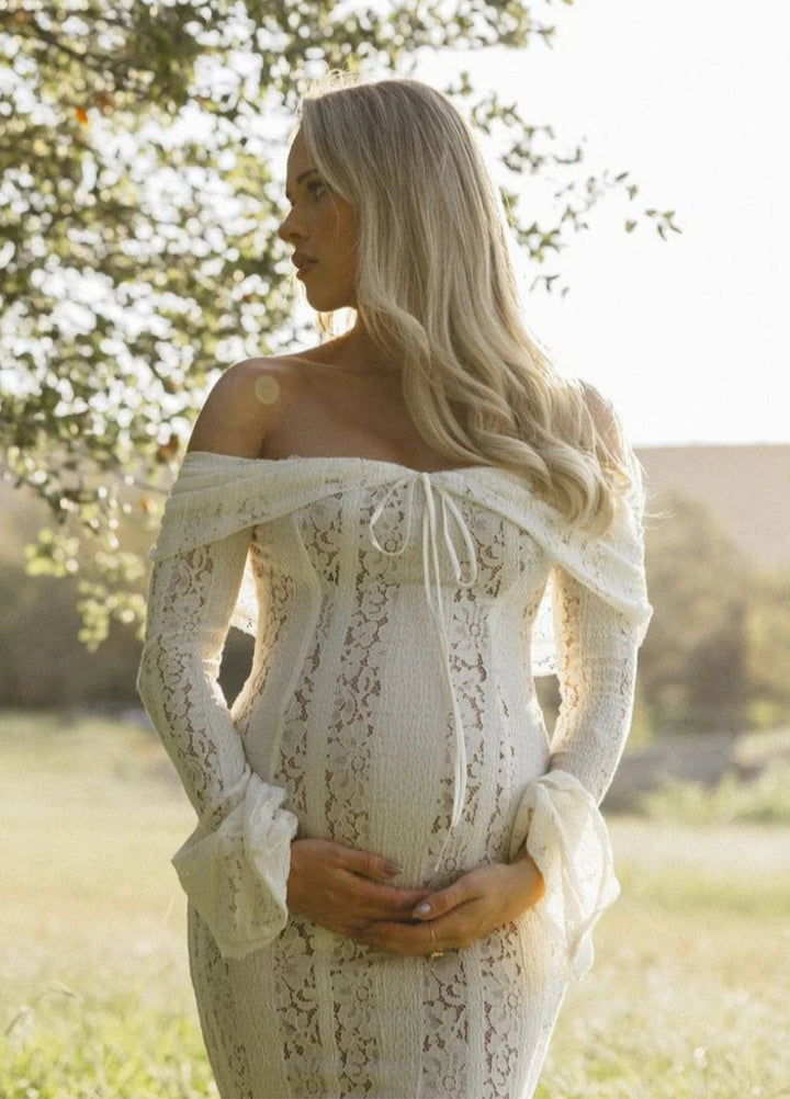 White lace maxi dress, off-shoulder neckline and long sleeves; fitted bodice, flowing skirt.