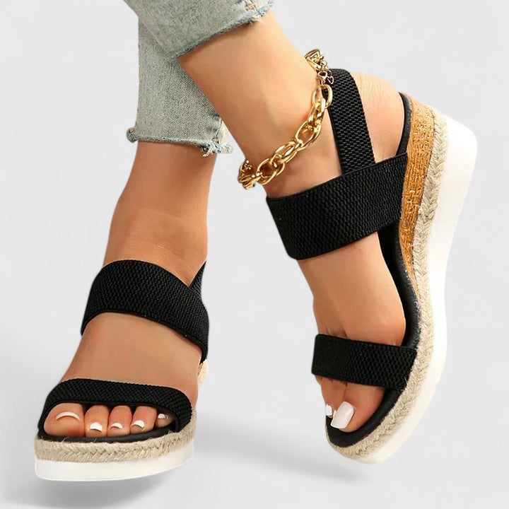 Orthopedic sandals with black straps and cork-look wedge sole, gold chain ankle bracelet