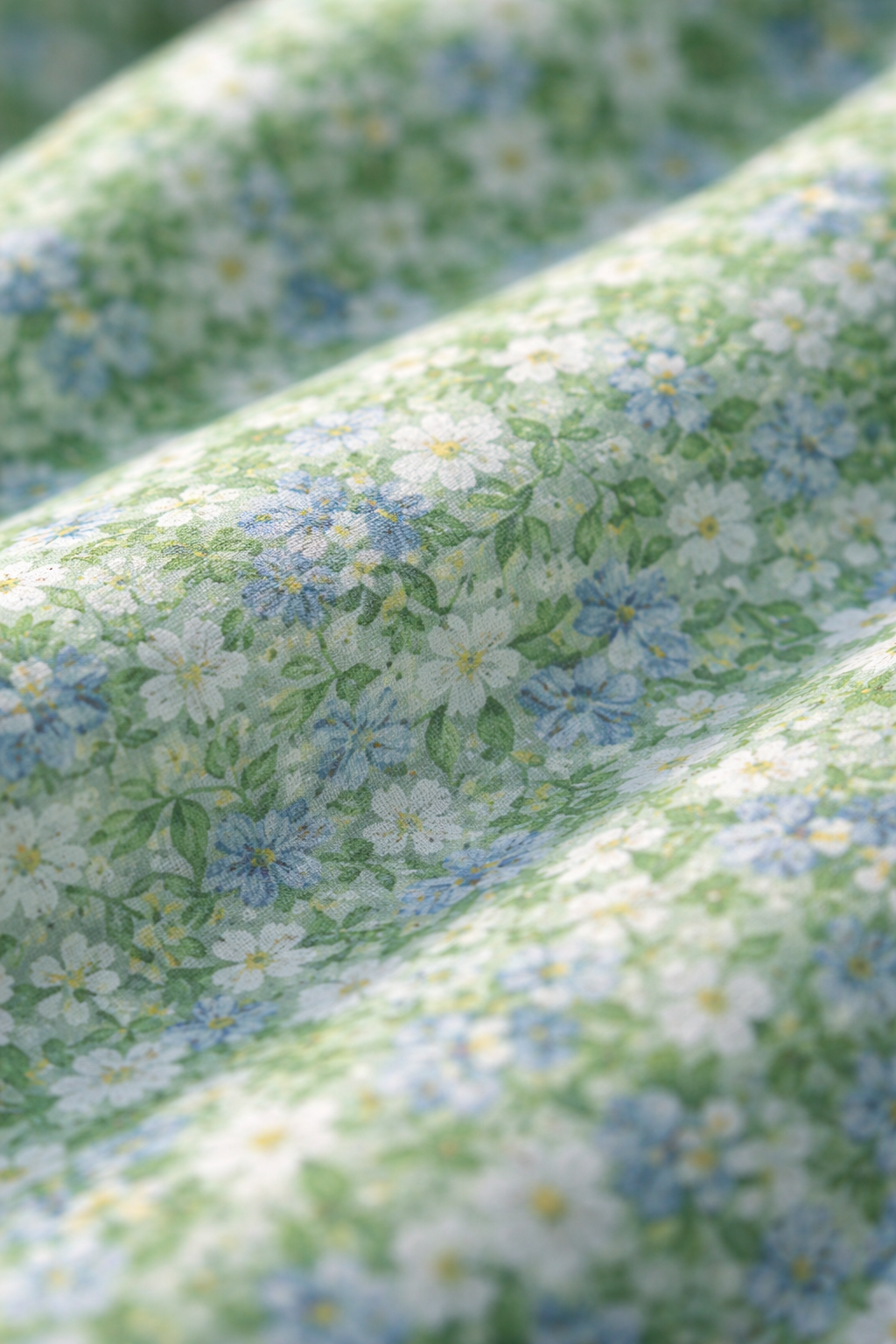 Light green floral fabric close-up with small white daisies and blue accents
