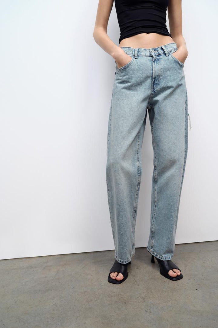 Light wash distressed denim jeans with wide legs, front patch details, frayed edges