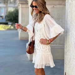 White embroidered lace mini dress with sheer sleeves, buttoned bodice, tiered hem