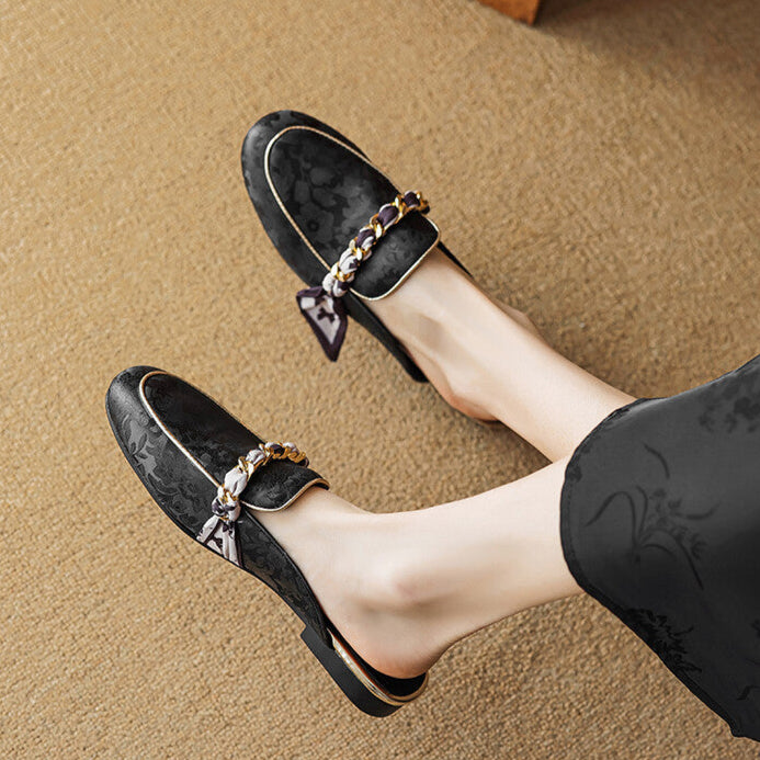 Black leather mules with chain-link bow detail and low slip-on silhouette