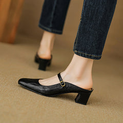 Black leather mule showing side view, low block heel, and buckle strap