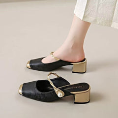 Black genuine leather mules with block heel, chain strap, and round pearl embellishment.