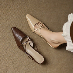 Beige and brown genuine leather mules with crisscross straps and mid heels, side view.