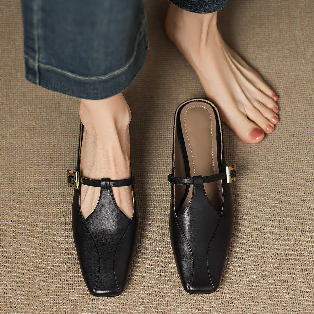 Black leather mules with open toe strap, gold buckle, and low block heel on feet