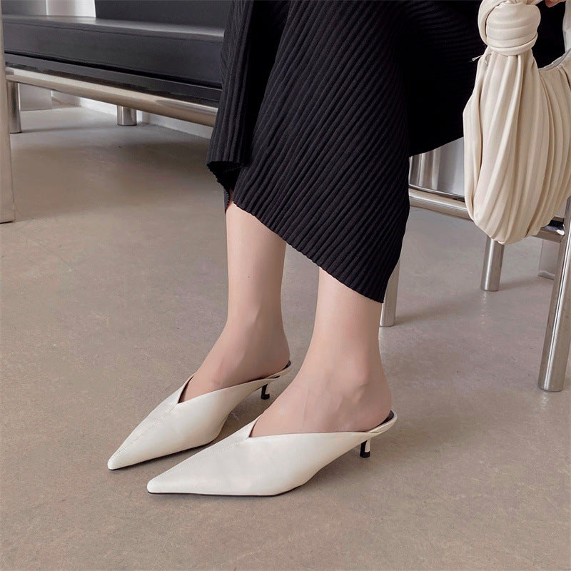 White pointed-toe mules with low heel worn with dark knit skirt