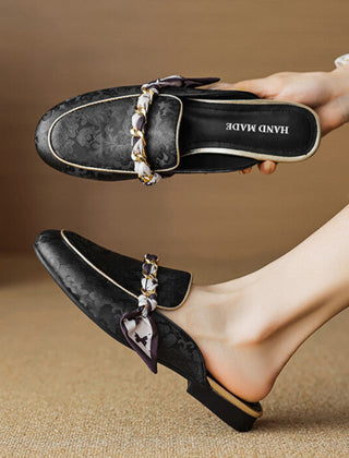 Black patterned leather mules with gold chain trim and bow detail, slip-on style