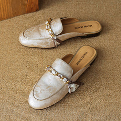 Pair of beige patterned leather mules with gold chain detail and bow at the strap