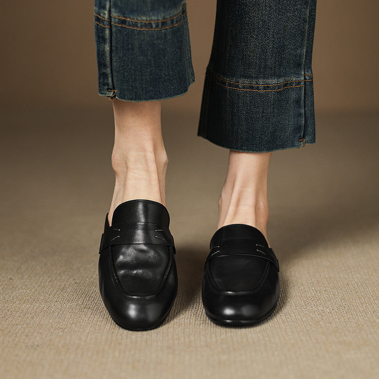 Black leather mules on feet, slip-on design with vamp strap and flat sole