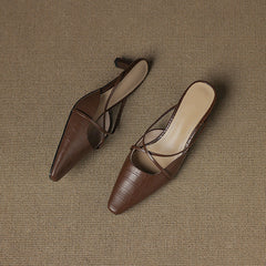 Pair of brown genuine leather mules with crisscross straps and mid heel, laid down.