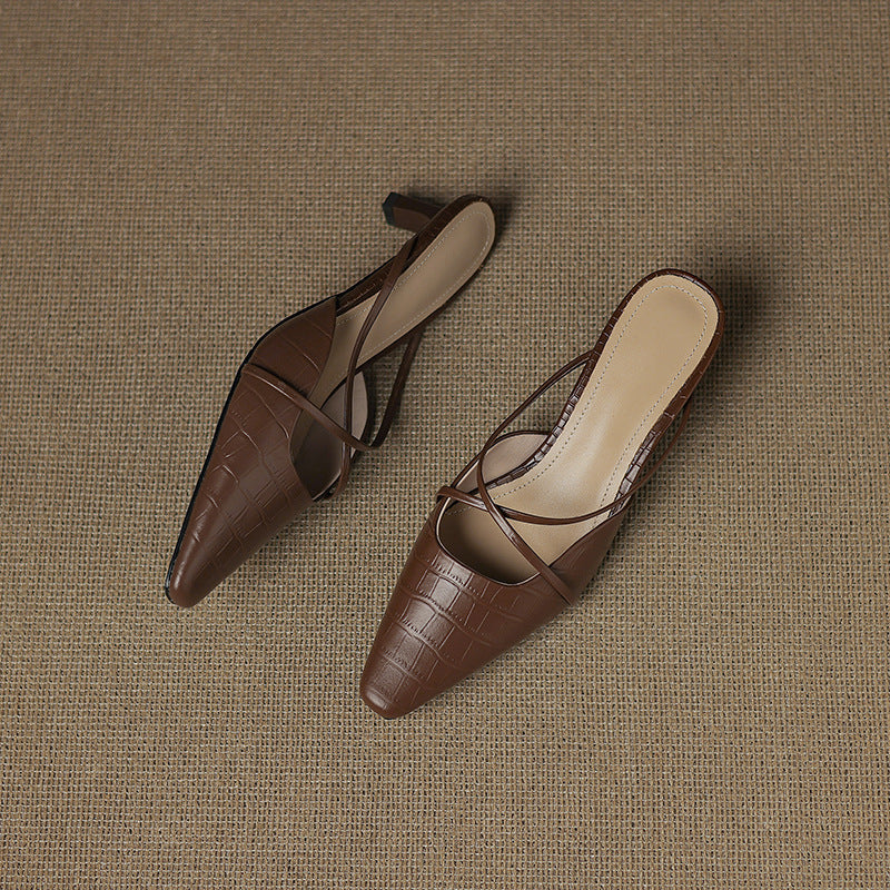 Pair of brown genuine leather mules with crisscross straps and mid heel, laid down.