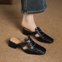 Black leather mule with buckle strap and low block heel worn on foot