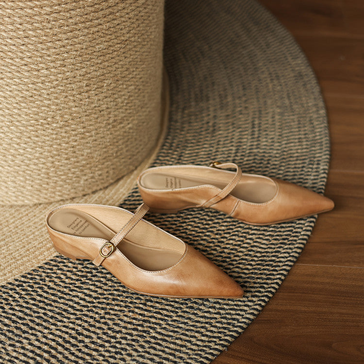 Tan leather pointed-toe mules with ankle strap buckle, shown on a textured rug