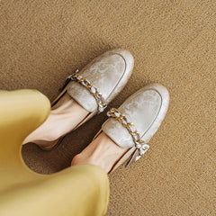 Beige patterned leather mules with gold chain across the upper and tied bow