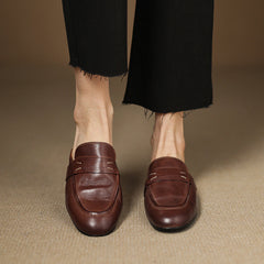 Two brown leather mules on feet, square toe slip-on with strap detail