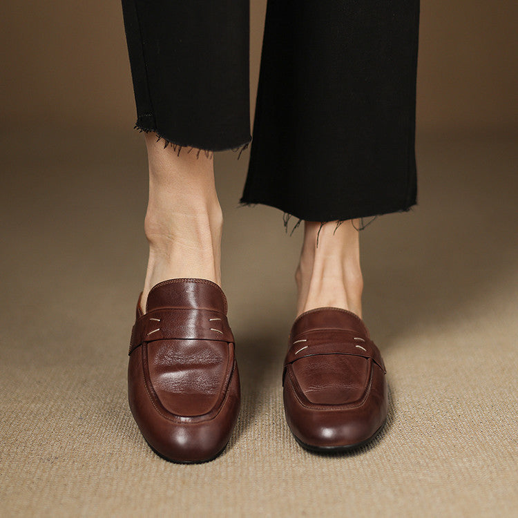 Two brown leather mules on feet, square toe slip-on with strap detail