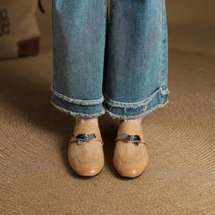 Tan leather mules with square toe and metallic buckle strap on denim jeans