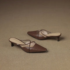 Brown genuine leather mules with crisscross straps and mid heel, pair on surface.
