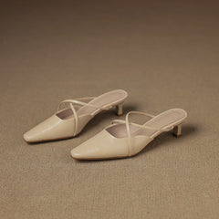 Two beige pointed-toe mules with crisscross straps and low block heel