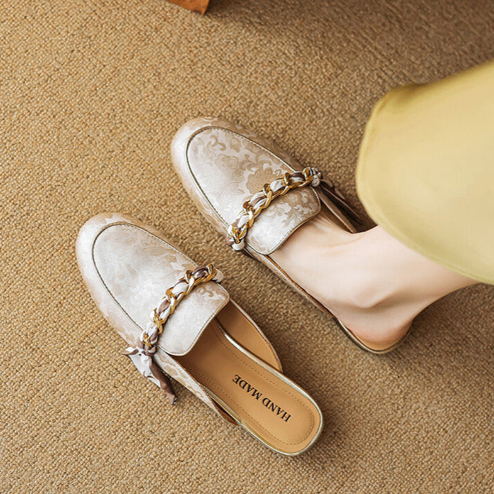 Beige patterned leather mules worn with gold chain trim and bow at the vamp