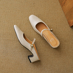 Pair of beige leather mules with low block heel and gold buckle strap.