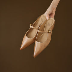 Tan leather mules held in hand, pointed toe and ankle strap with buckle